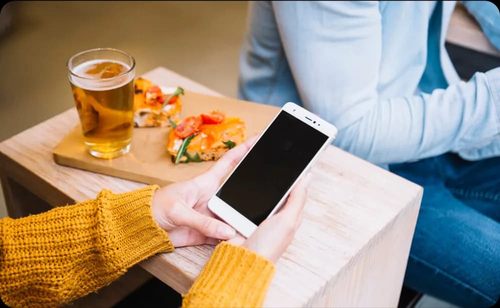 Customer using a smartphone to browse a digital menu and place an order through Eatsy Orders at a restaurant table.